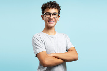 Portrait of positive handsome teenage boy wearing eyeglasses with crossed arms looking at camera