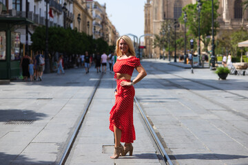 Young and beautiful blonde woman from the United States is on a sightseeing trip to Seville, Spain. The woman is enjoying her holidays in europe. She is between the rails of the urban tram.