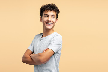 Portrait smiling handsome guy wearing braces with arms crossed posing isolated on beige background