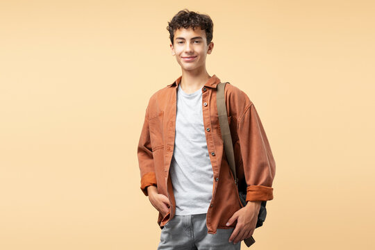 Portrait of smiling handsome teenage boy wearing brown shirt backpack looking at camera