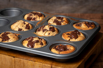 Homemade banana and chocolate muffins from the oven in a baking tray with melting chocolate.