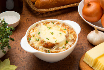 French onion soup in a white ceramic bowl on a brown table with ingredients. - 677274741