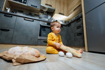 A little boy 1 year old is sitting in the kitchen with fresh bread. Child with bread on the floor.