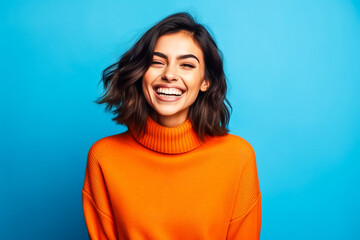 Jeune femme souriante portant un pull orange devant un fond bleu