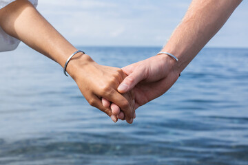 Close-up of the hands of a loving couple against the background of the sea and blue sky