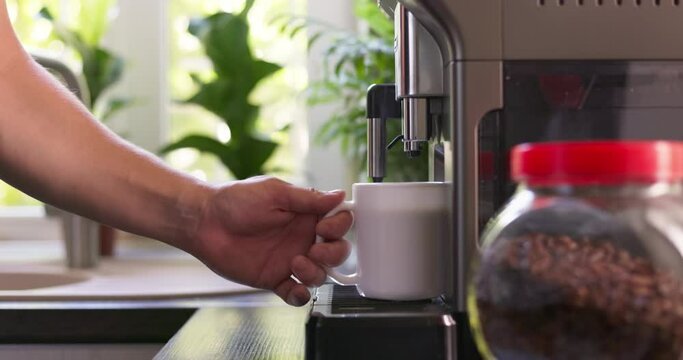 Male hand picking up a cup of coffee prepared by a coffee machine at home in the kitchen. Beverage drink for breakfast