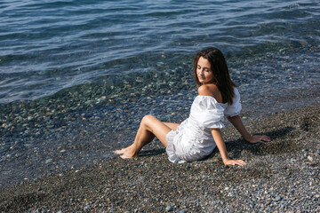 Fototapeta na wymiar Portrait of a girl from the back, sitting on a pebble beach by the sea, looking behind her