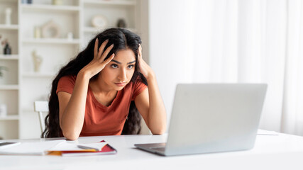 Exhausted indian woman sitting at workplace in front of laptop