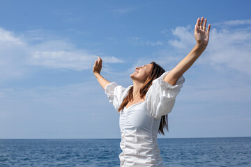 A young girl stands against the backdrop of the sea with her arms outstretched and her eyes closed