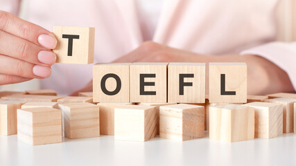 hand stacking wood cube block with toefl word on wooden table. business startup and entrepreneur...