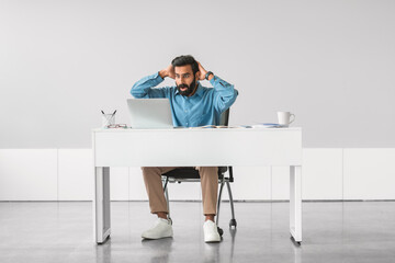 Stressed indian man at desk with laptop