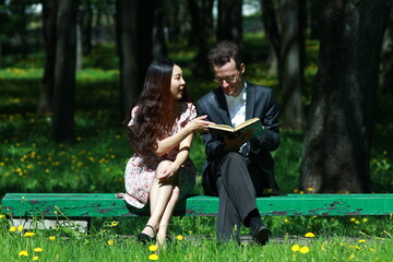 The international couple of the Asian girl and European man reading book on the bench in the park