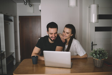 Positive young couple entertaining with laptop at home