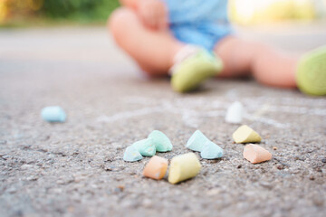 Crayons are lying on the asphalt next to the foot of a small child
