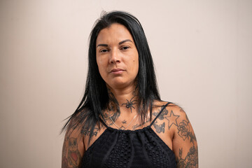Young tattooed woman looking seriously at the camera on a pastel background.