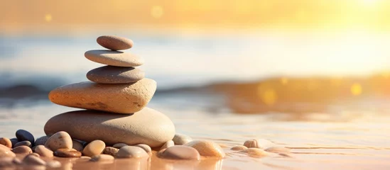 Tuinposter Balanced rock pyramid on pebbled beach with golden sea bokeh Zen stones on sea beach conveying meditation spa harmony and balance Copy space image Place for adding text or design © Ilgun
