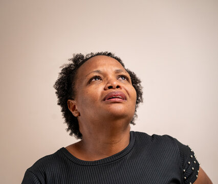 Black Woman Looking Up With Sad Expression On Pastel Background.