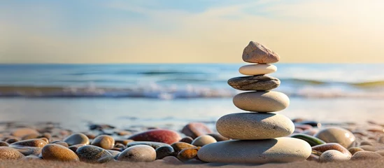 Fotobehang Stenen in het zand Balanced rock pyramid on pebbled beach with golden sea bokeh Zen stones on sea beach conveying meditation spa harmony and balance Copy space image Place for adding text or design