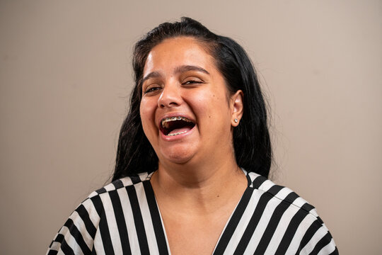 Young Brunette Woman With Braces Smiling On Pastel Background.