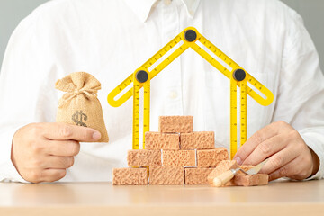 Businessman hand holding a folding ruler in the shape of a house and money bag in the office, Loan...