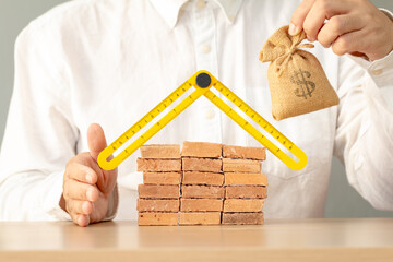 Businessman hand holding a folding ruler in the shape of a house and money bag in the office, Loan...