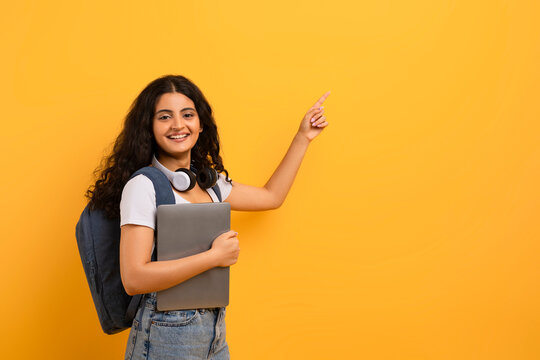 Cheerful indian woman student with laptop pointing at copy space