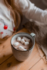 cute little girl in Santa hat and pajamas drinks cocoa with marshmallows in the kitchen at home on Christmas day