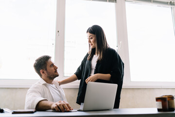 Cheerful colleagues discussing at table with laptop