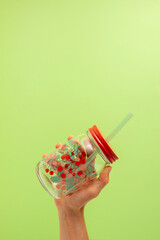 hand taking a transparent glass with flowers and a drinking straw on a green background. Copy space