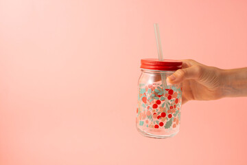 hand taking a transparent glass with flowers and a drinking straw on a pink background. Copy space