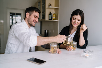 Cheerful man pouring tea into glass of woman