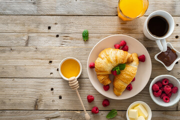 Continental breakfast with croissants, orange juice and cup of coffee on wooden table with copy...
