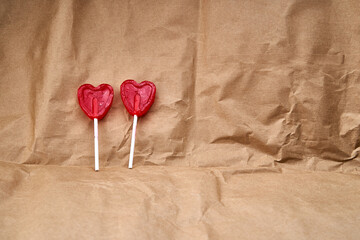 Two red heart-shaped lollipops together representing love, on a cardboard textured background.
