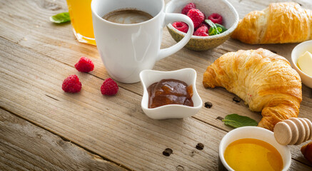Continental breakfast with croissants, orange juice and cup of coffee on wooden table with copy space. Healthy breakfast eating, various morning food concept