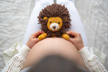 Close-up of a cute, excited, stuffed toy lion sitting on the mother's naked, round belly. Last...