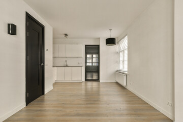 an empty room with white walls and wood flooring on the right side, there is a black door in the left corner