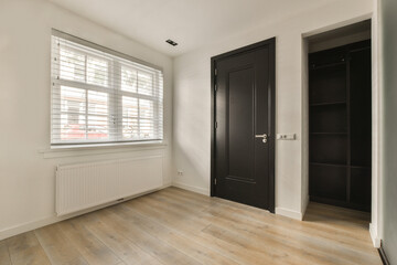 an empty room with white walls and wood flooring, there is a black door that leads to another room