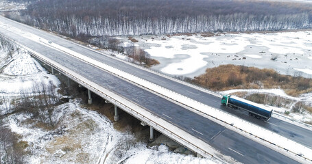 Aerial winter traffic. Drone countryside road. Snowy bridge trough frozen lake asphalted icy danger...