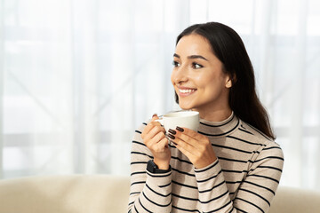 Cheerful young arab woman drink cup of hot coffee, tea in light living room, kitchen interior