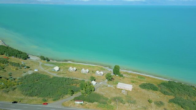 Aerial view of houses and boats, trees, beach big blue azure lake sea in clear sunny weather. Drone video, flying in an arc. Lake Sevan, Armenia.