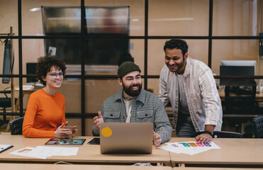 Cheerful colleagues sitting at table while working on project with laptop in office