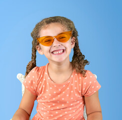 Sitting young girl with big smile wearing vintage style orange glasses isolated on blue background - 677333901