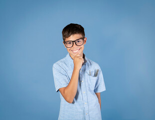 Cute adolescent boy student wearing nerd glasses hand on chin isolated on blue background - 677333945