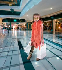 Sassy spoiled little girl shopper wearing orange scarf with bored attitude at the mall holding shopping bags - 677333959