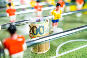 Close up shot of a roll of euro money bills placed on the green plastic field of a table football game, concept of European football, transfers, betting and gambling - obrazy, fototapety, plakaty