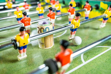 Yellow plastic football player kicking ball with a roll of euro bank notes aside on the table football game