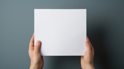 Female hands holding a blank white paper sheet on a gray background.