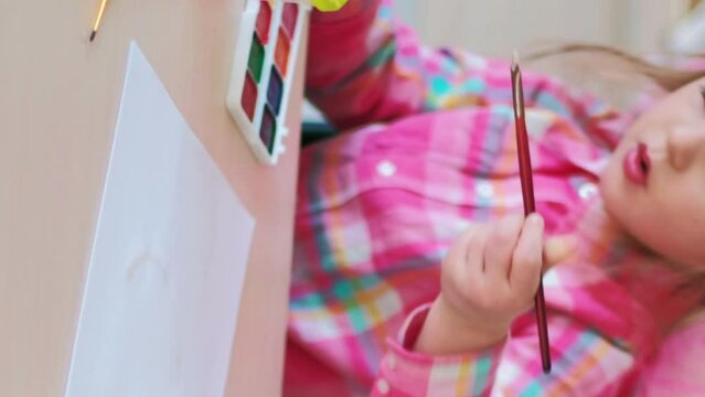 Vertical video. Art preschool. Children creativity. Focused little girl enjoying painting on paper with watercolor at desk at kids hobby space.
