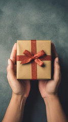 Female hands holding a gift box with a red bow on dark background.