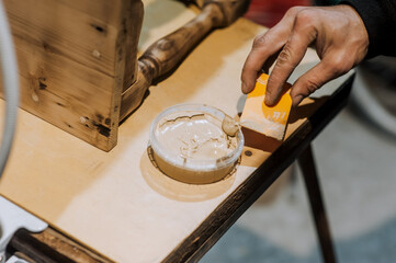 Male professional worker carpenter, woodworker smears putty with plastic spatula, cement on a wooden chair in the workshop. Photography, handmade concept.